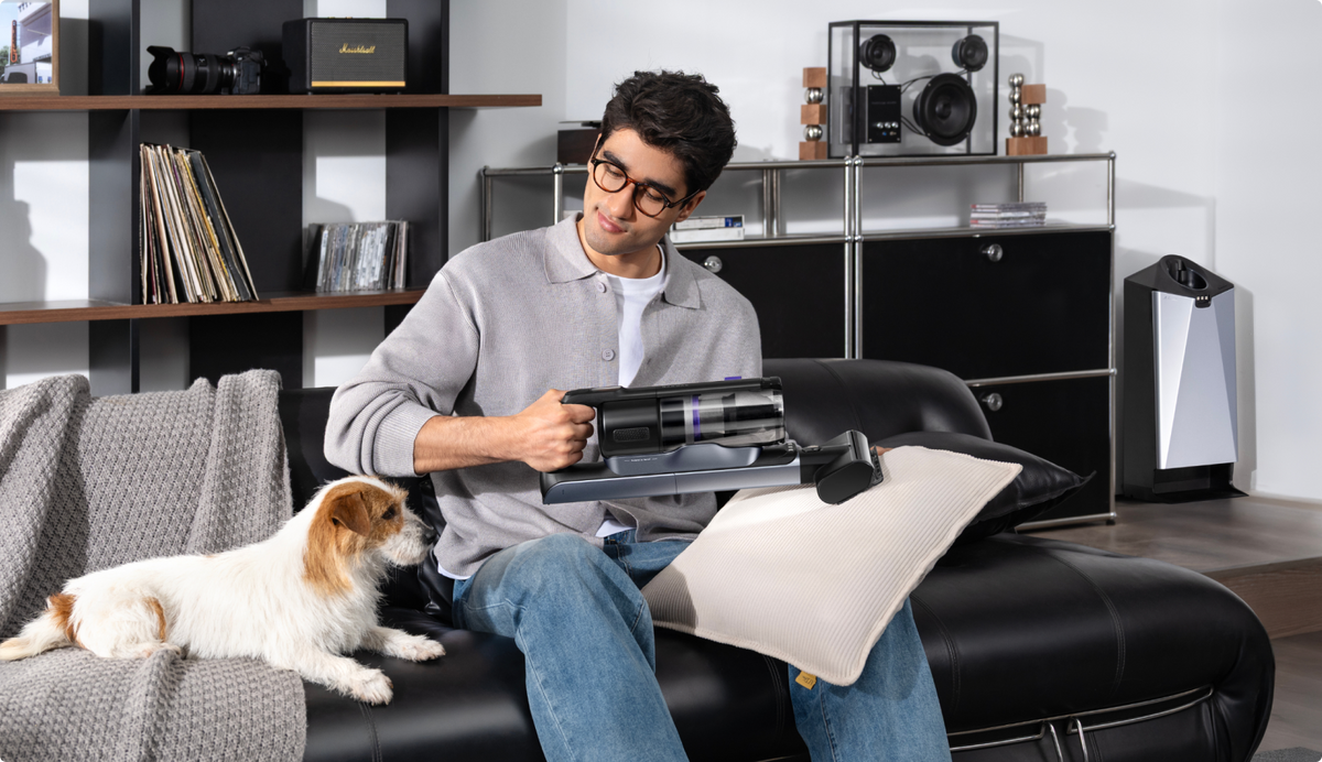 Man cleaning a sofa cushion with the Narwal V50 Cube hand tool beside a dog