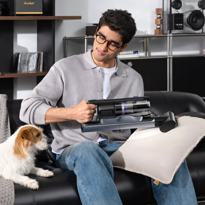 Man cleaning a sofa cushion with the Narwal V50 Cube hand tool beside a dog
