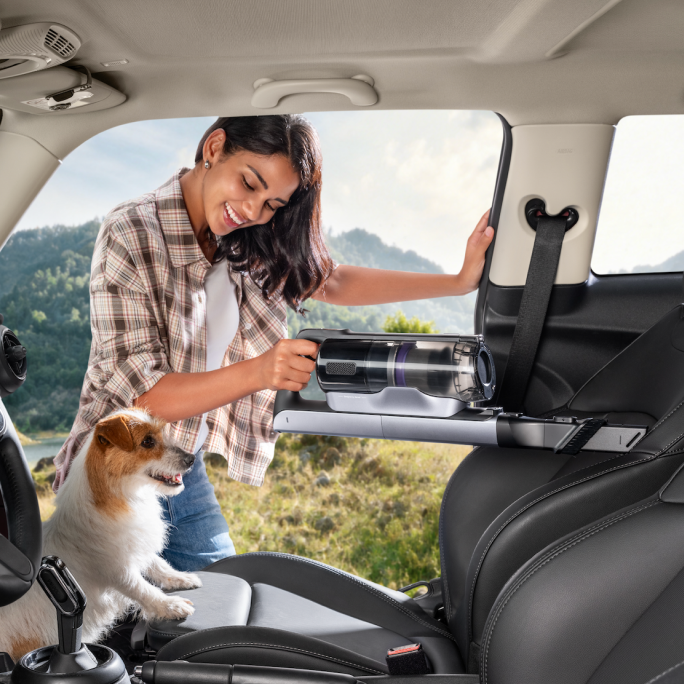 Woman cleaning a car interior with the Narwal V50 Cube crevice tool beside a dog
